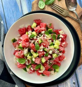 overhead view white bowl with watermelon feta salad garnished with fresh basil and mint leaves