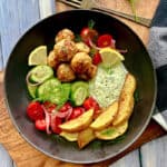 overhead view - black bowl with air fryer meatballs, diced tomatoes and cucumbers, potato wedges and yogurt feta dip