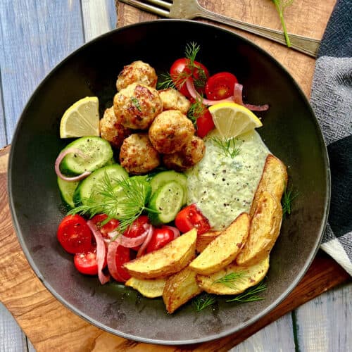 overhead view - black bowl with air fryer meatballs, diced tomatoes and cucumbers, potato wedges and yogurt feta dip