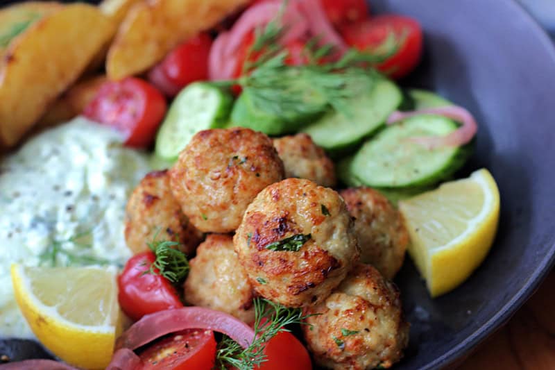 black bowl with closeup of air fryer meatballs along with potatoes and sliced cucumber and tomatoes