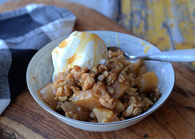 white bowl with apple crisp and a scoop of vanilla ice cream
