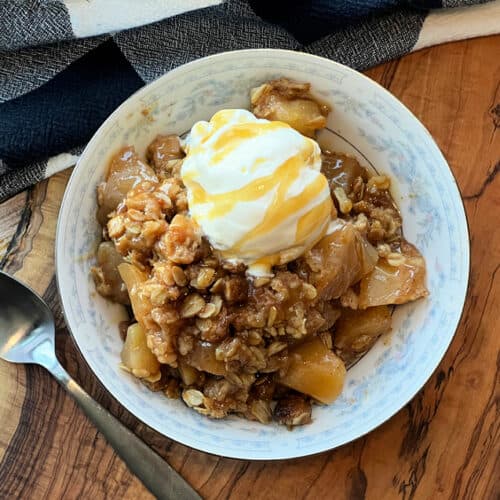 white bowl with apple crisp, a scoop of vanilla ice cream and caramel drizzle