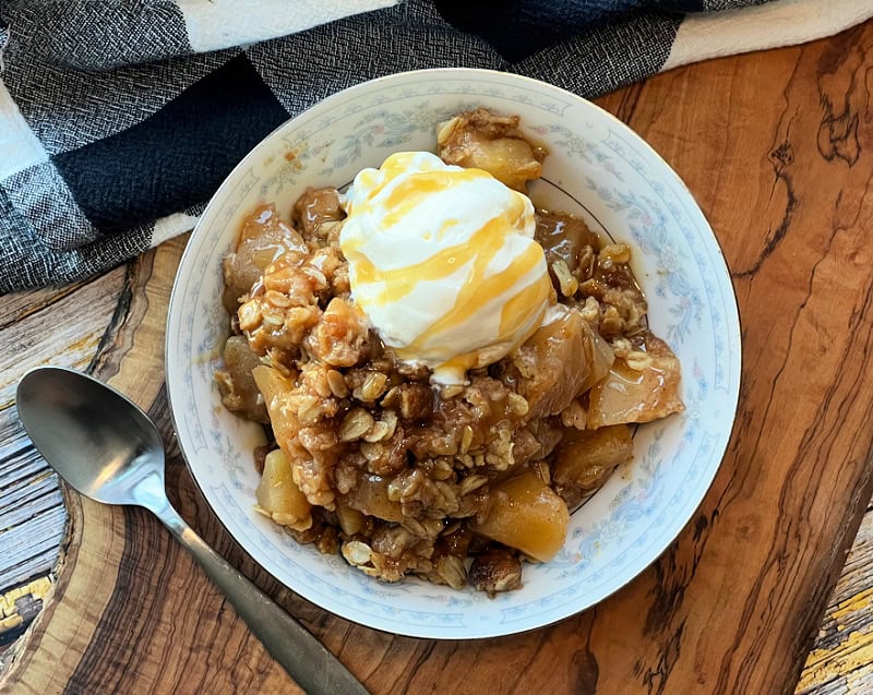white bowl with apple crisp, a scoop of vanilla ice cream and caramel drizzle