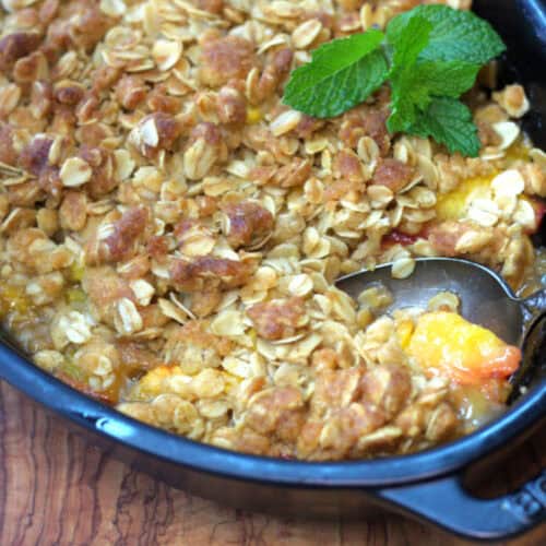 close up of peach crisp in black baking dish with spoon scooping some out