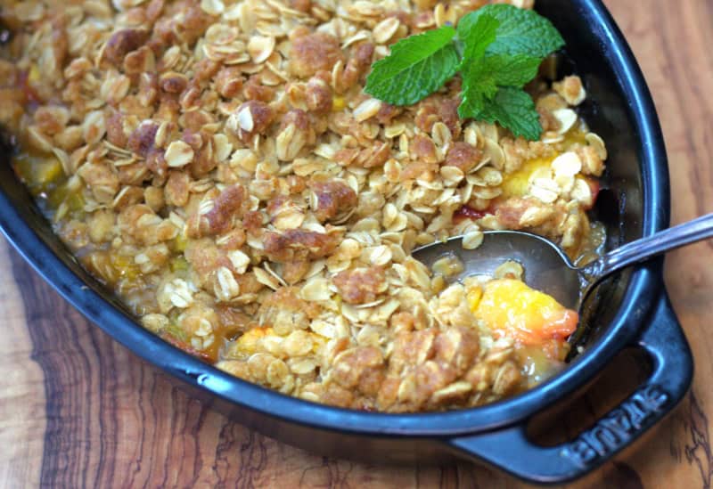 close up of peach crisp in black baking dish with spoon scooping some out