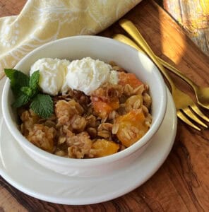 white bowl with peach crisp topped with scoops of vanilla ice cream