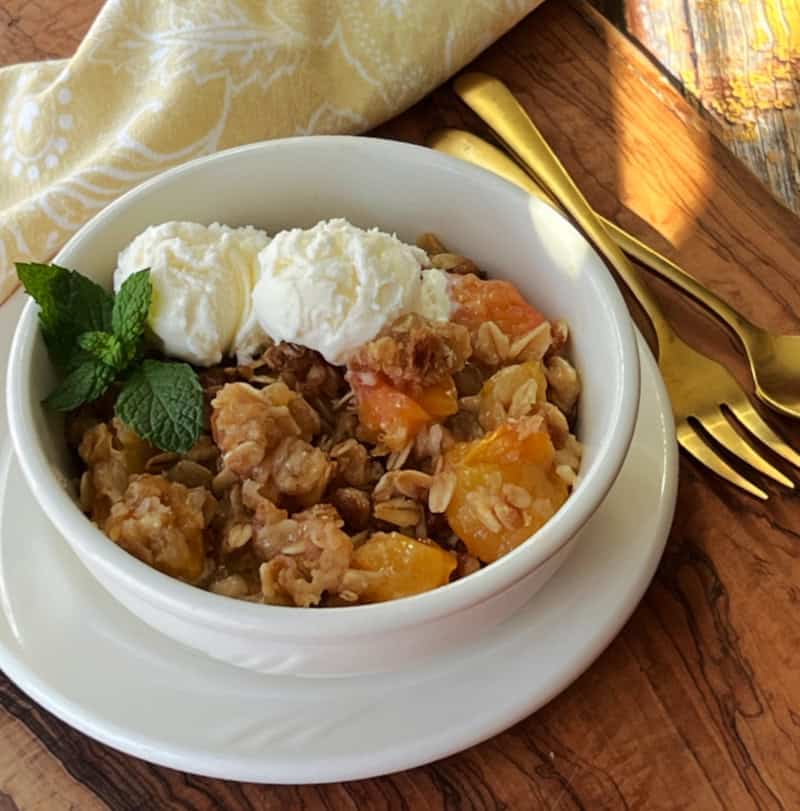 white bowl with peach crisp topped with scoops of vanilla ice cream