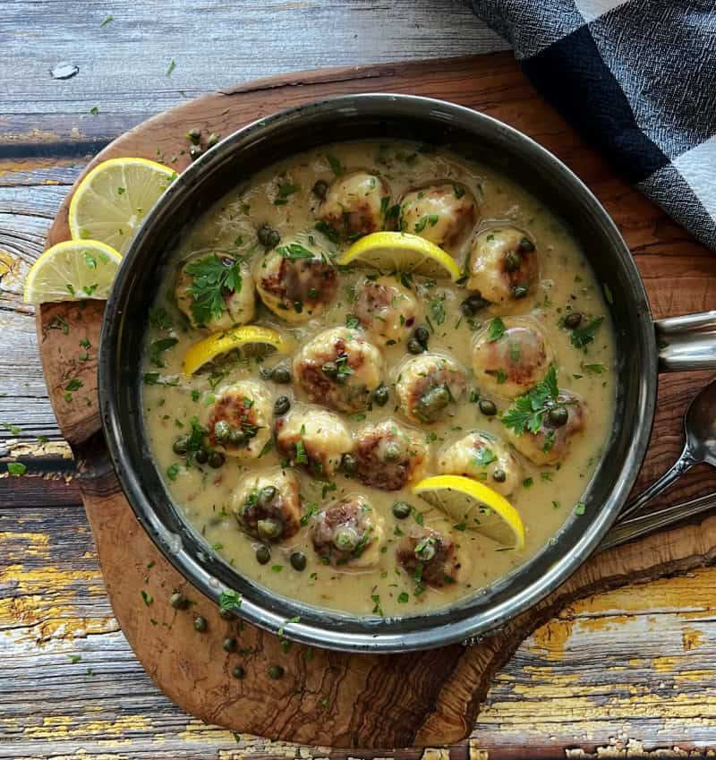 overhead view skillet with chicken piccata meatballs garnished with lemonslices