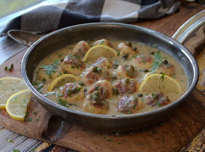 skillet with chicken piccata meatballs garnished with lemon slices and chopped parsley
