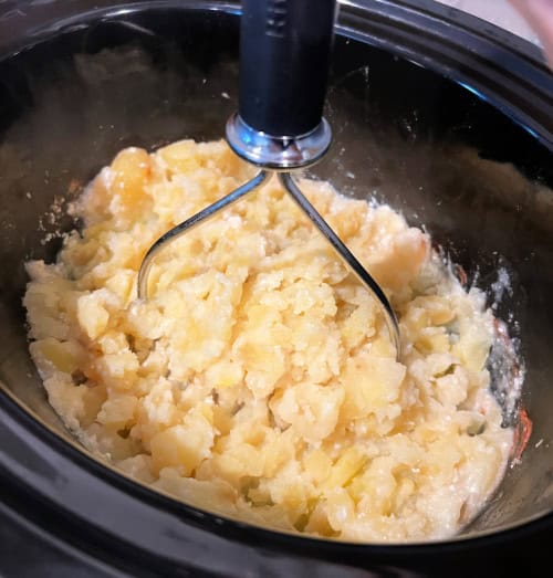 potatoes being mashed in crockpot for slow cooker mashed potatoes