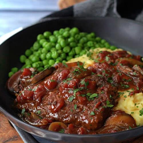 shallow black bowl with swiss steak, mashed potatoes and gravy and green peas