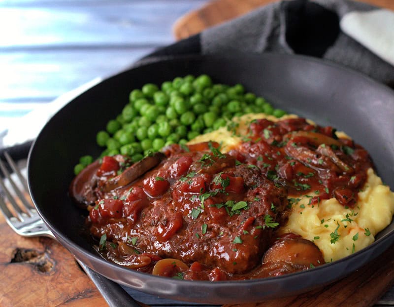black bowl with swiss steak, mashed potatoes, gravy and peas