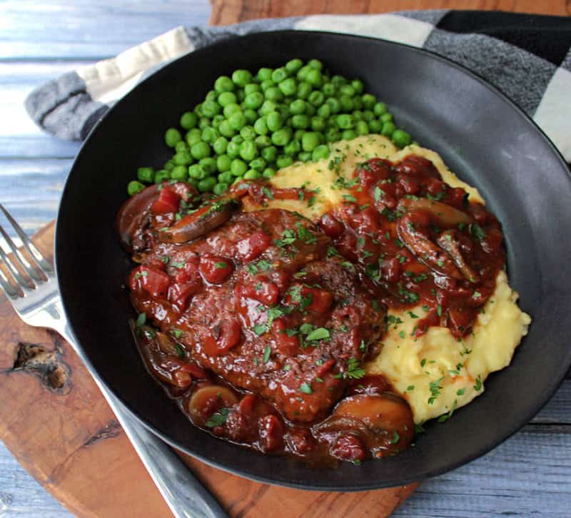 overhead view of black bowl with swiss steak, mashed potatoes, gravy and peas