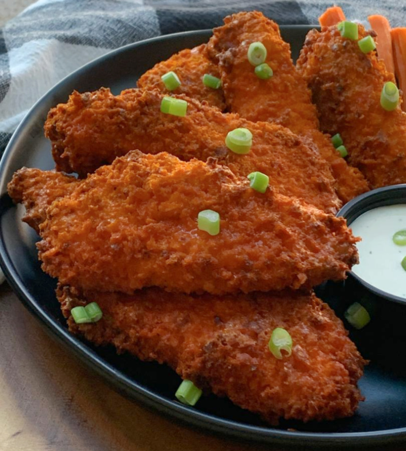 closeup - black plate with air fryer buffalo chicken tenders garnished with sliced green onions