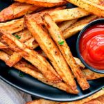 black plate with golden fries and side of ketchup