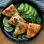 overhead view black plate quartered quesadillas with sliced avocado