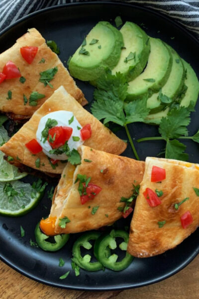 overhead view black plate quartered quesadillas with sliced avocado