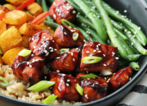 black plate with air fryer teriyaki salmon bites, green beans and brown rice