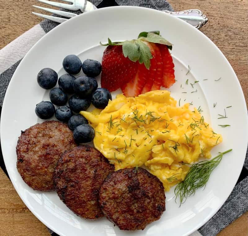overhead view white plate, 3 air fryer sausage patties, scrambled eggs and fresh fruit