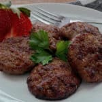 white plate with air fryer sausage patties and a sliced strawberry