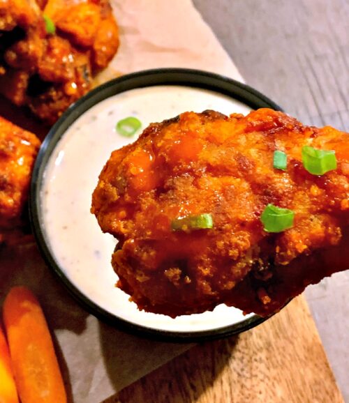closeup of one air fryer chicken wing dipping into bowl of ranch dressing.