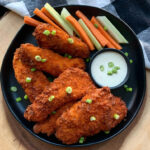 black plate with air fryer buffalo chicken tenders, ranch dressing and sliced carrots and celery