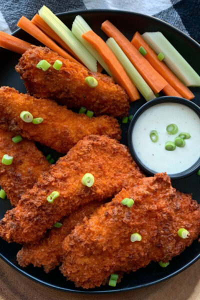 black plate with air fryer buffalo chicken tenders, ranch dressing and sliced carrots and celery
