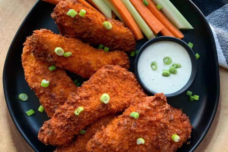 black plate with air fryer buffalo chicken tenders, ranch dressing and sliced carrots and celery