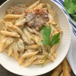 overhead view white bowl, penne pasta with alfredo sauce and sliced chicken