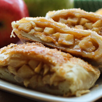 sliced easy apple strudel on white plate with whole apples in background