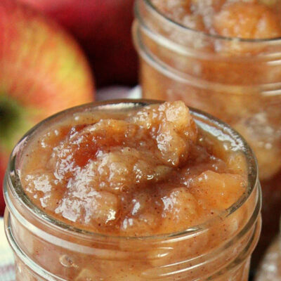 mason jar filled with slow cooker applesauce and apples in background