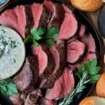 black plate with sliced roast beef tenderloin and side of blue cheese sauce