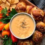 bowl of beer cheese dip surrounded by vegetables and pretzel bites