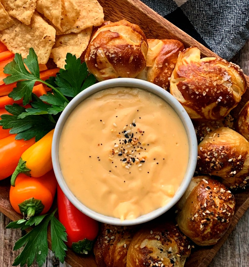bowl of beer cheese dip surrounded by vegetables and pretzel bites