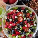 white bowl with summer berry salad with mixed greens and smaller bowls of fresh berries