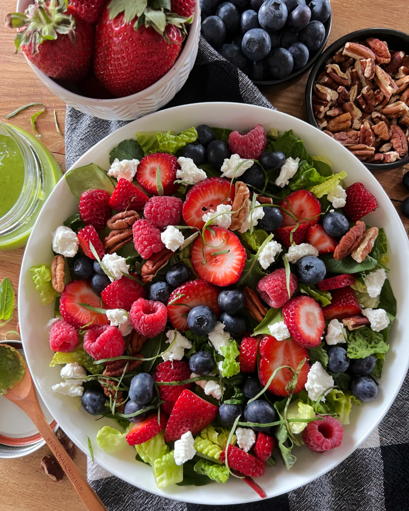white bowl with summer berry salad with mixed greens and smaller bowls of fresh berries