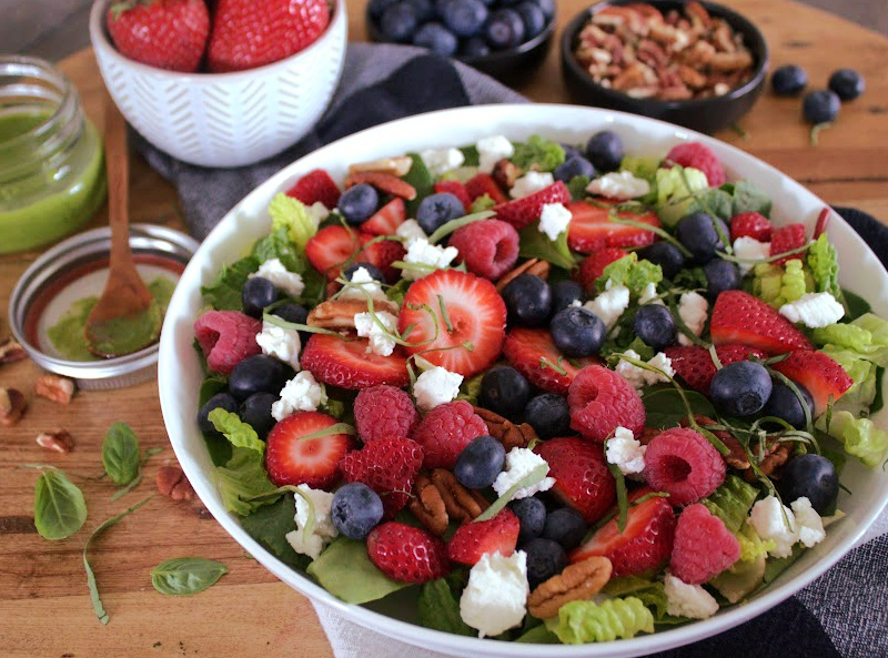 white bowl with summer berry salad with mixed greens and smaller bowls of fresh fruit