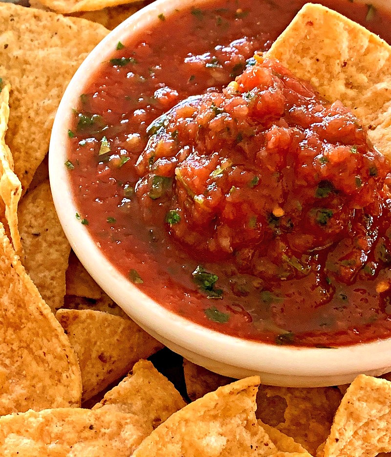 restaurant style salsa in a white bowl surrounded by tortilla chips