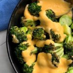 Roasted Broccoli topped with homemade cheese sauce on black plate