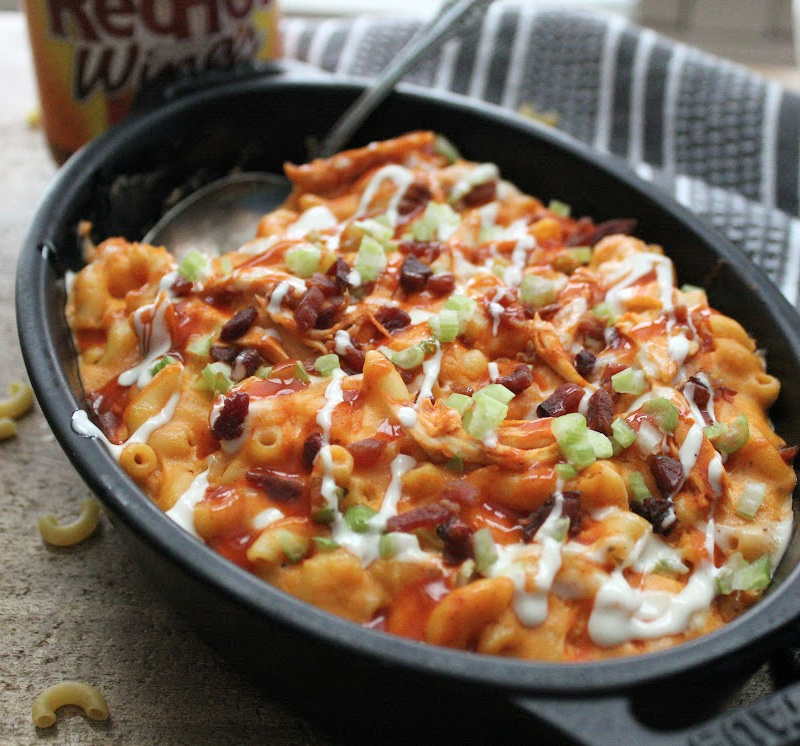 black baking dish with buffalo chicken mac and cheese garnished with bacon and blue cheese