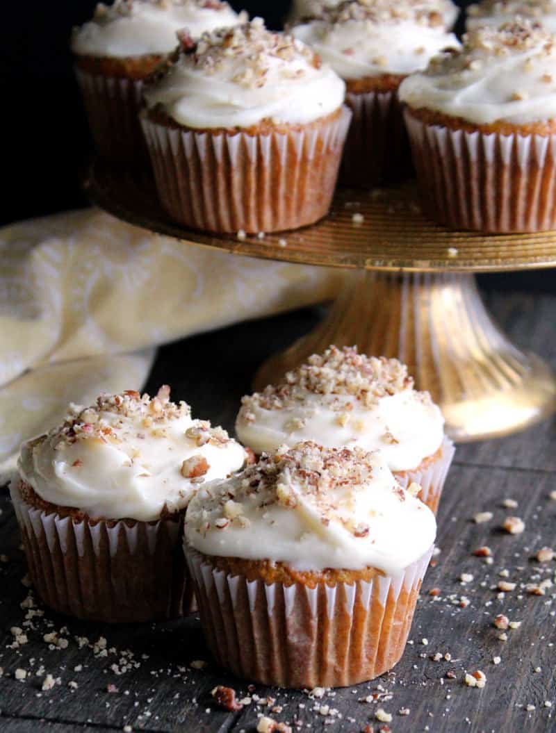 carrot cake cupcakes ~ easy recipe from scratch shows cream cheese frosted cupcakes sprinkled with finely chopped pecans.
