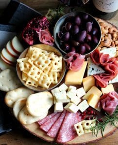 large round board loaded with cheese, charcuterie and crackers