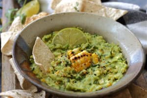 brown bowl with charred corn with guacamole and tortilla chip scooping out guacamole