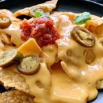 black plate with tortilla chips and homemade cheese sauce spooned over the top.