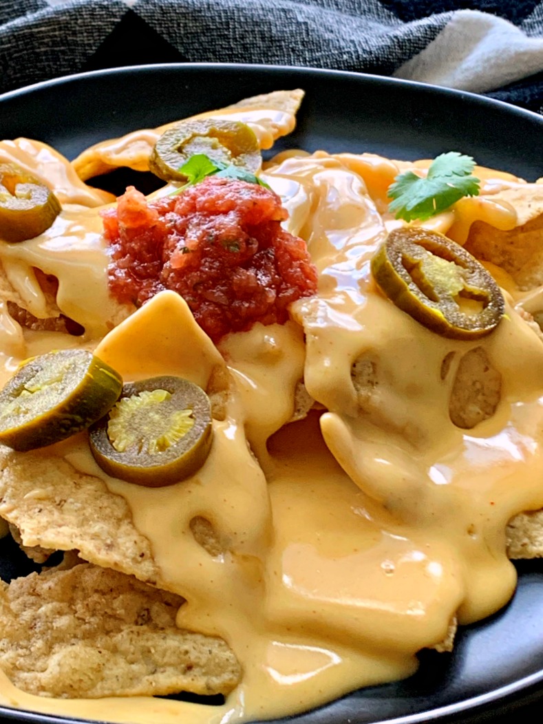 plate of nachos with cheese sauce on top garnished with jalapenos
