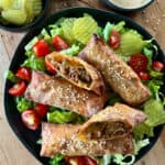 Overhead view black plate with air fryer cheeseburger egg rolls on a bed of lettuce