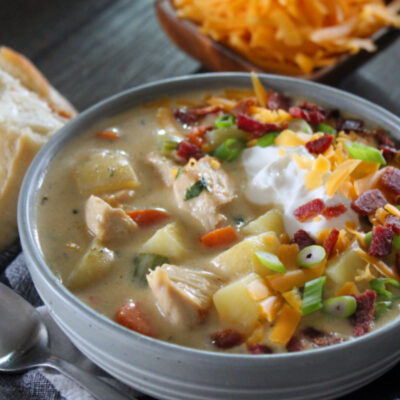 gray bowl with creamy chicken potato soup garnished with bacon and shredded cheese