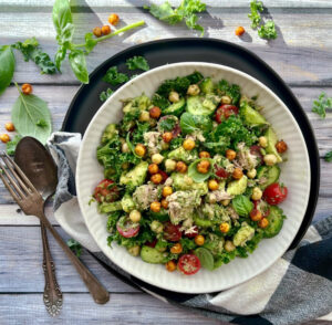 overhead view white bowl with Avocado Chickpea Tuna Salad garnished with small basil leaves.