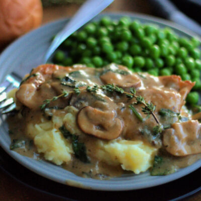 gray plate with chicken dijon with mushrooms, mashed potatoes and green peas.