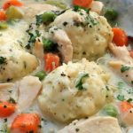 drop dumplings in a bowl of chicken and dumplings with carrots, garnished with parsley
